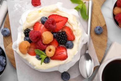 Photo of Pavlova cake (meringue dessert) with whipped cream, fresh berries and mint on table, flat lay