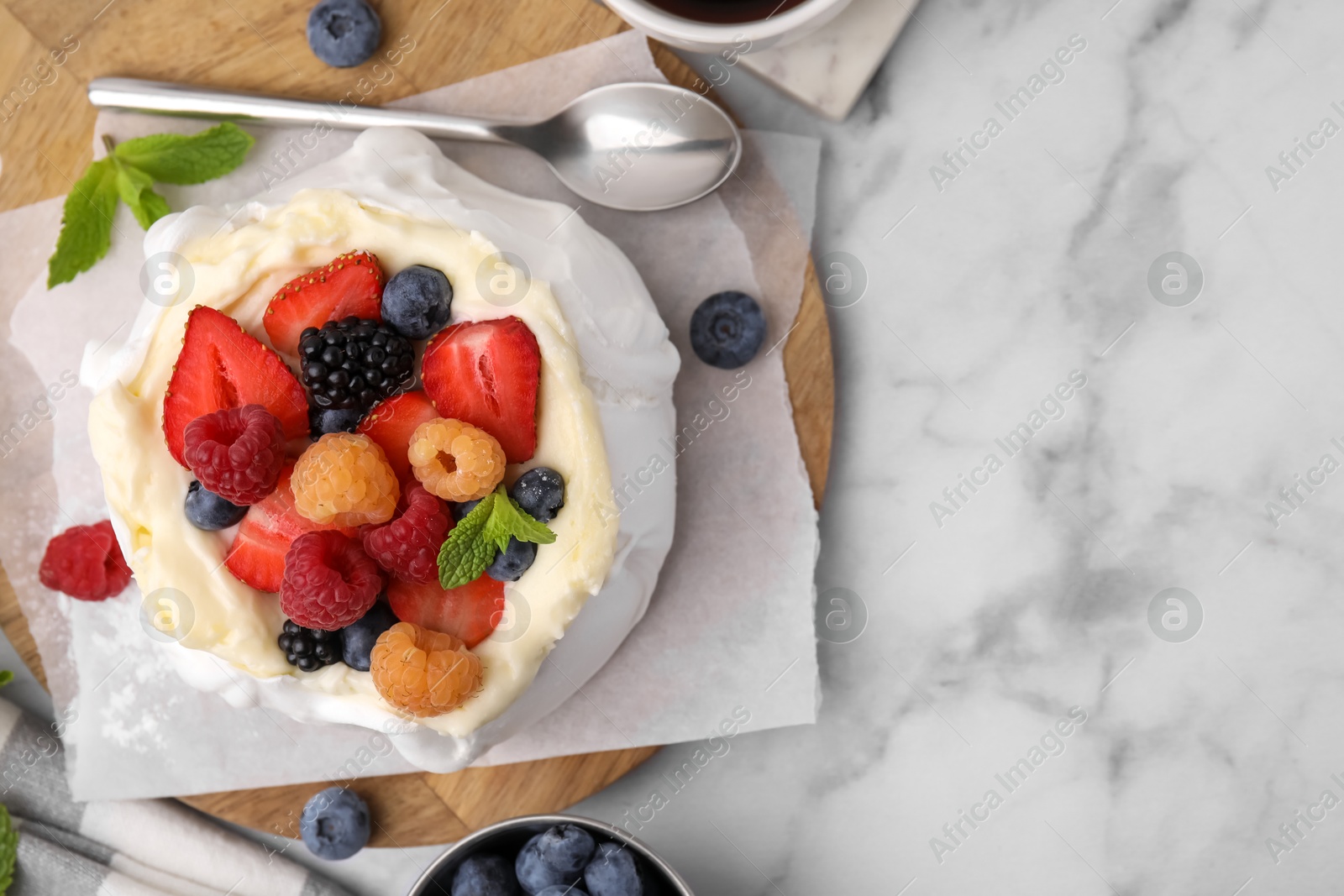 Photo of Pavlova cake (meringue dessert) with whipped cream, fresh berries and mint on white marble table, flat lay. Space for text