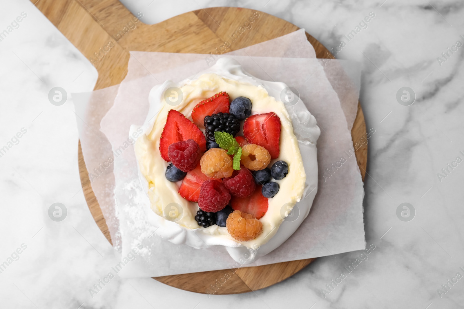 Photo of Pavlova cake (meringue dessert) with whipped cream, fresh berries and mint on white marble table, top view