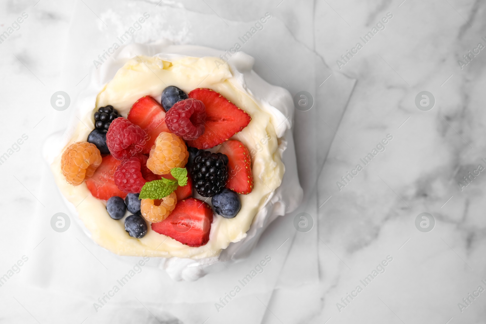 Photo of Pavlova cake (meringue dessert) with whipped cream, fresh berries and mint on white marble table, top view. Space for text