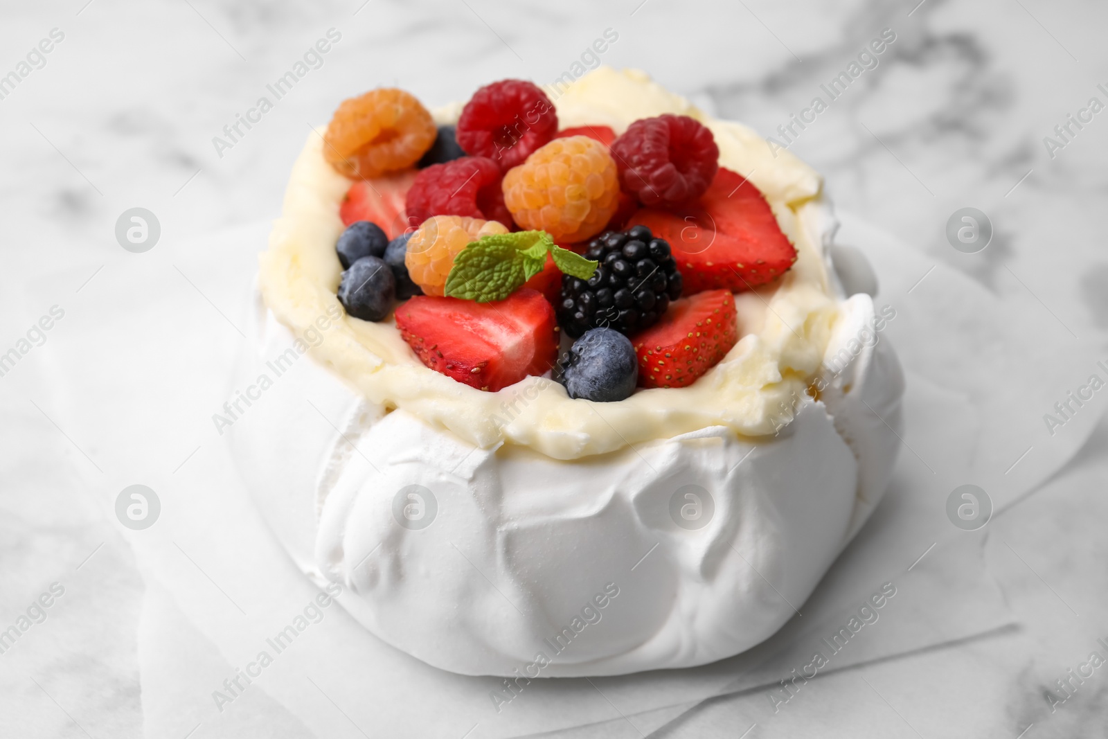 Photo of Pavlova cake (meringue dessert) with whipped cream, fresh berries and mint on white marble table, closeup