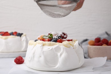 Photo of Woman sprinkling powdered sugar onto Pavlova cake (meringue dessert) at table, closeup