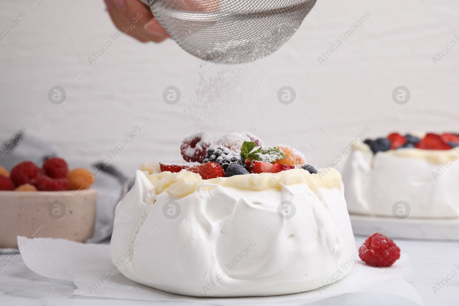 Photo of Woman sprinkling powdered sugar onto Pavlova cake (meringue dessert) at table, closeup