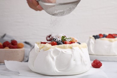 Photo of Woman sprinkling powdered sugar onto Pavlova cake (meringue dessert) at table, closeup