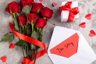 Sorry card in envelope, gift box and red roses on grey table, top view