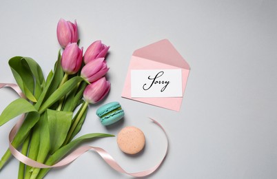 Sorry card, envelope, macarons and pink tulips on light grey table, flat lay. Space for text