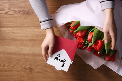 Woman with sorry card and bouquet of flowers at wooden table, closeup