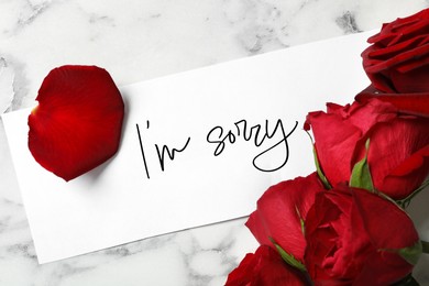 Sorry card and red roses on white marble table, above view