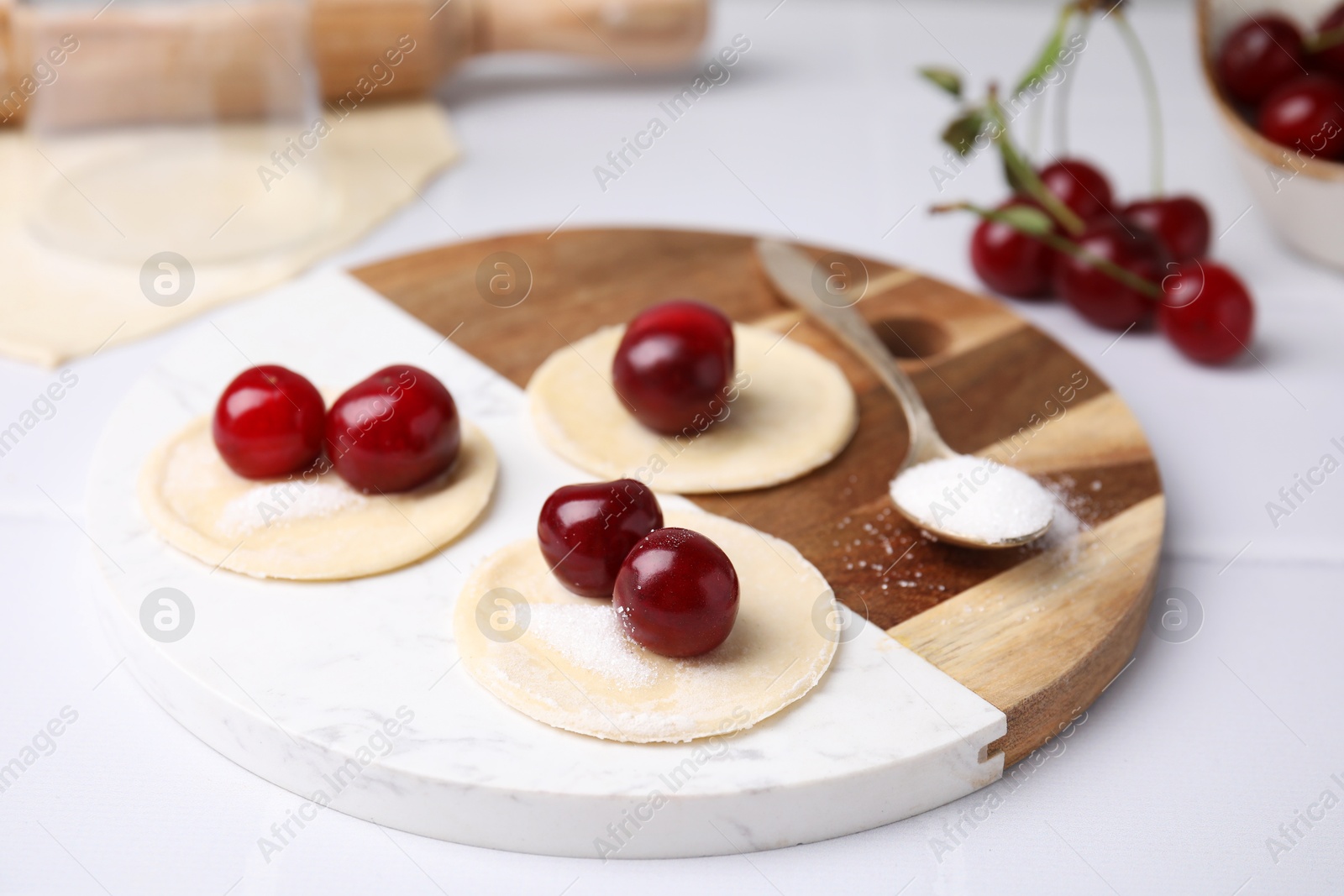 Photo of Process of making dumplings (varenyky) with cherries. Raw dough and ingredients on white table, closeup