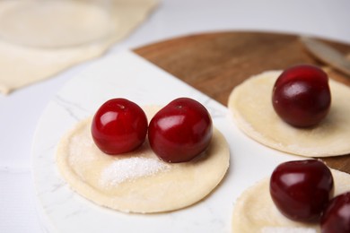 Photo of Process of making dumplings (varenyky) with cherries. Raw dough and ingredients on white table, closeup