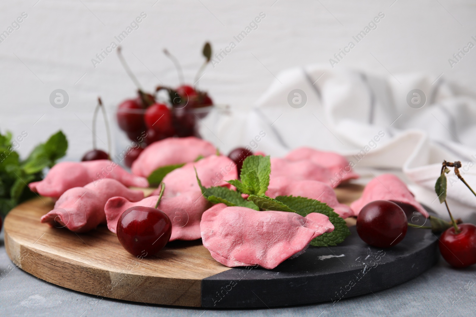 Photo of Raw dumplings (varenyky), fresh cherries and mint on grey table