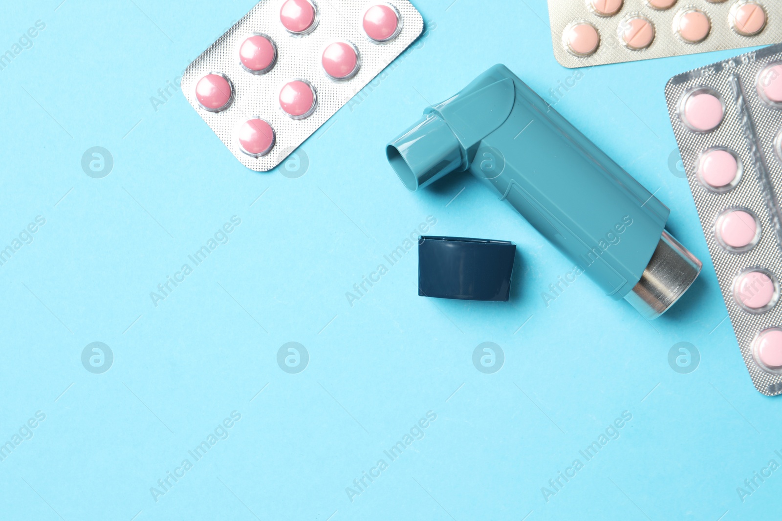 Photo of Asthma inhaler and pills on light blue background, flat lay. Space for text