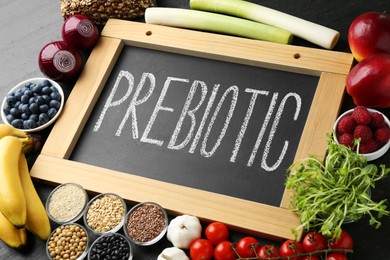 Photo of Chalkboard with word Prebiotic and different fresh products on black table