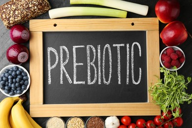 Photo of Chalkboard with word Prebiotic and different fresh products on black table, flat lay