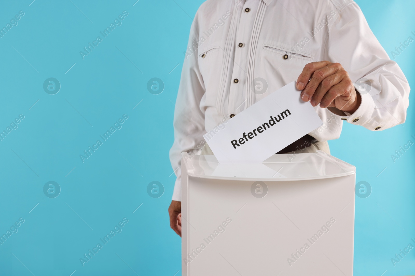 Photo of Referendum. Man putting his vote into ballot box against light blue background, closeup