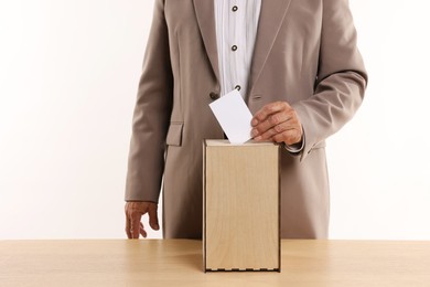 Photo of Referendum. Man putting his vote into ballot box at wooden table against white background, closeup