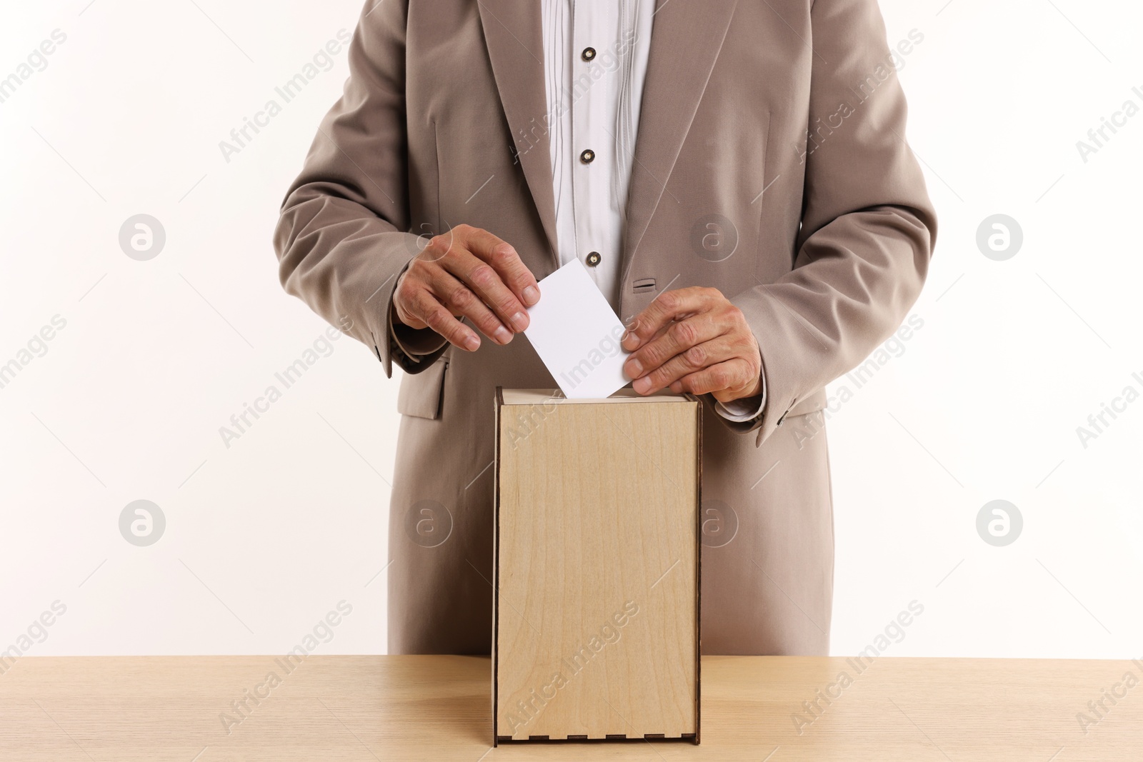 Photo of Referendum. Man putting his vote into ballot box at wooden table against white background, closeup