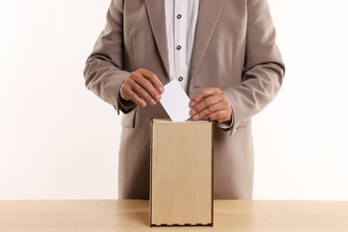 Photo of Referendum. Man putting his vote into ballot box at wooden table against white background, closeup