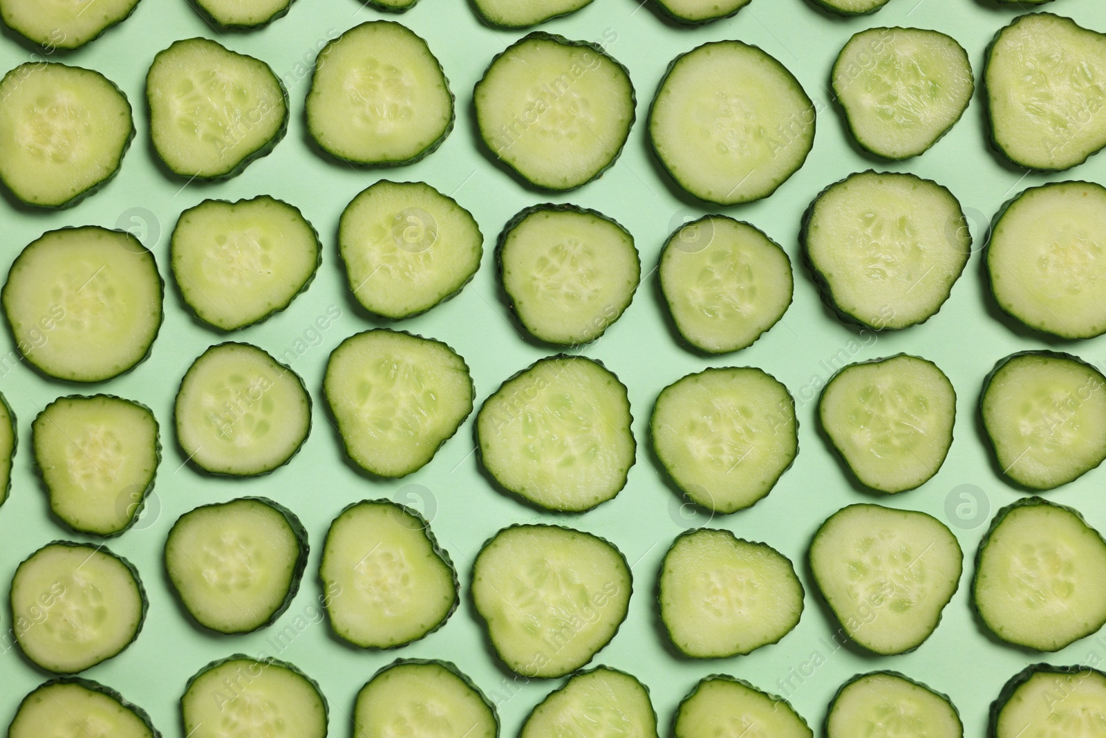 Photo of Slices of fresh cucumbers on turquoise background, flat lay