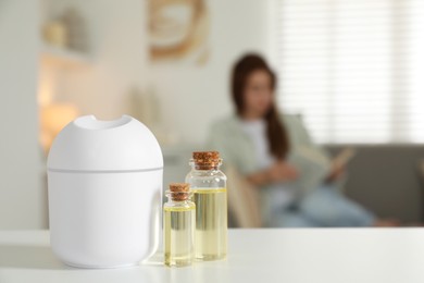 Photo of Woman reading book at home, focus on aroma diffuser and bottles of essential oils