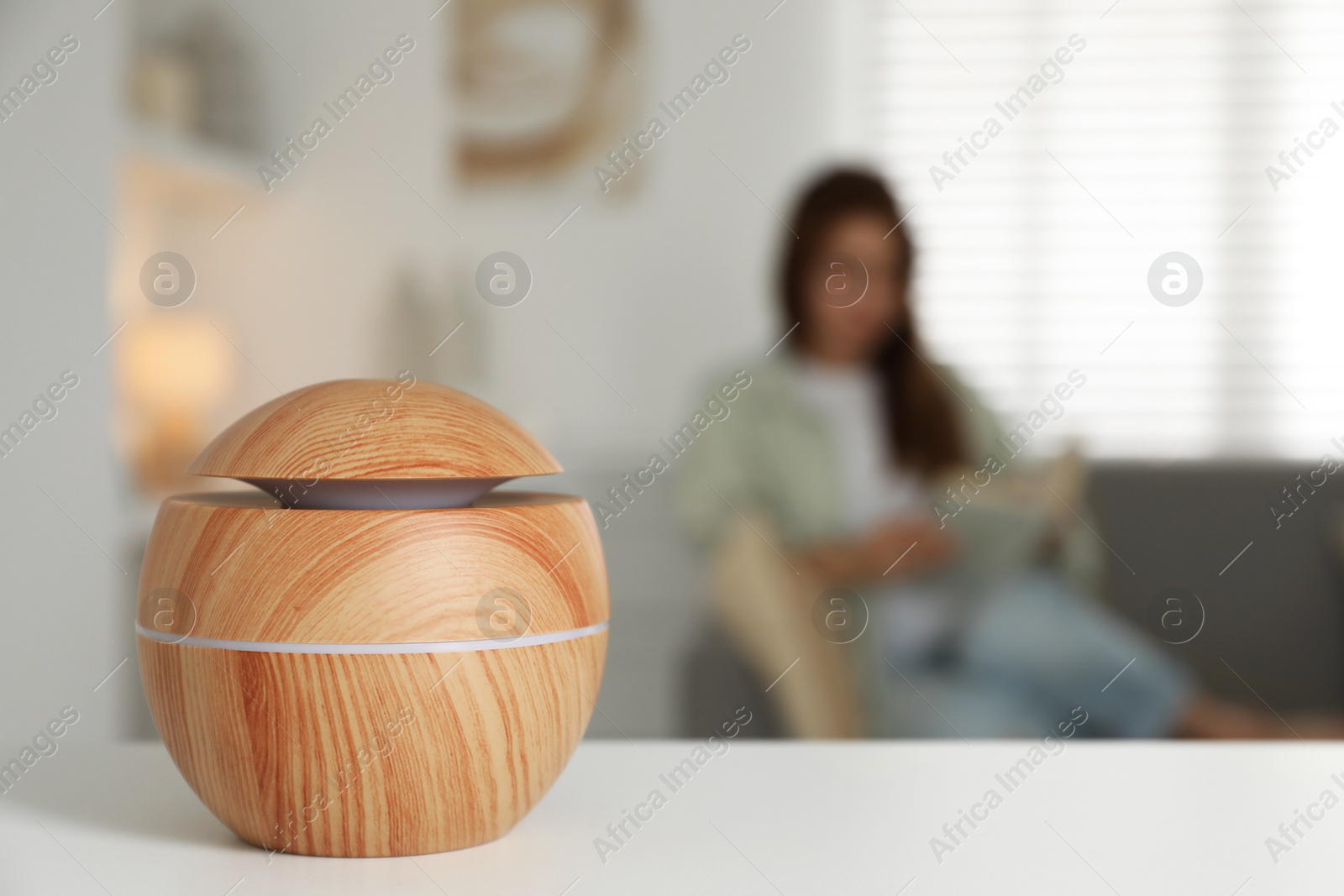 Photo of Woman reading book at home, focus on essential oil aroma diffuser