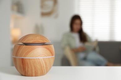 Photo of Woman reading book at home, focus on essential oil aroma diffuser