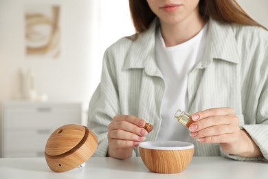 Photo of Woman adding essential oil to aroma diffuser at home, closeup