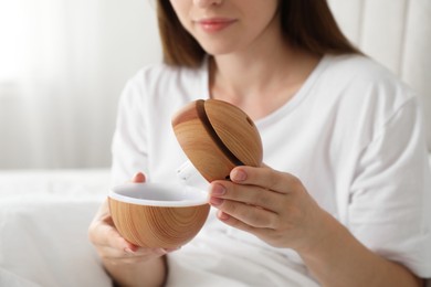 Photo of Woman with essential oil aroma diffuser at home, closeup