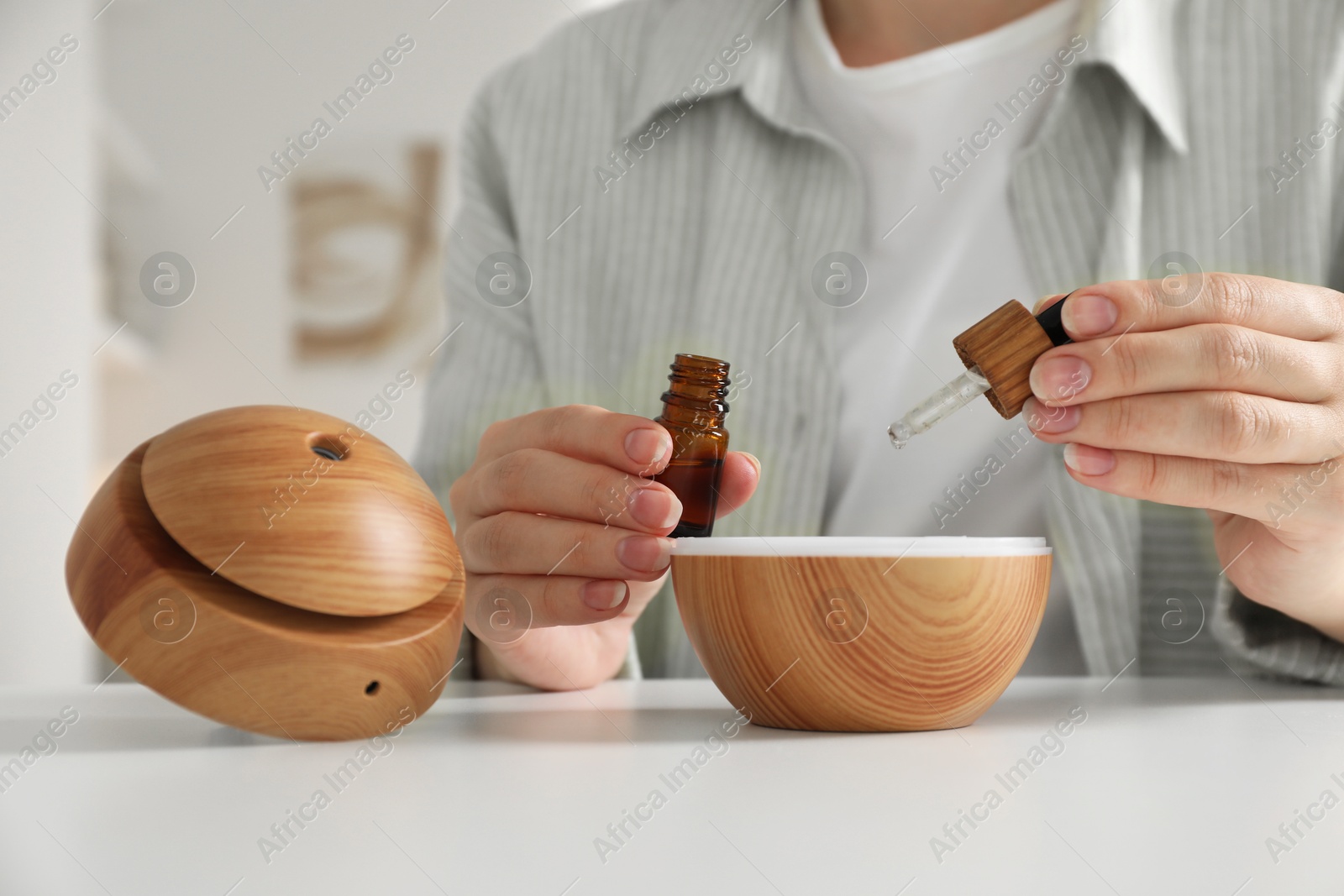 Photo of Woman adding essential oil to aroma diffuser at home, closeup