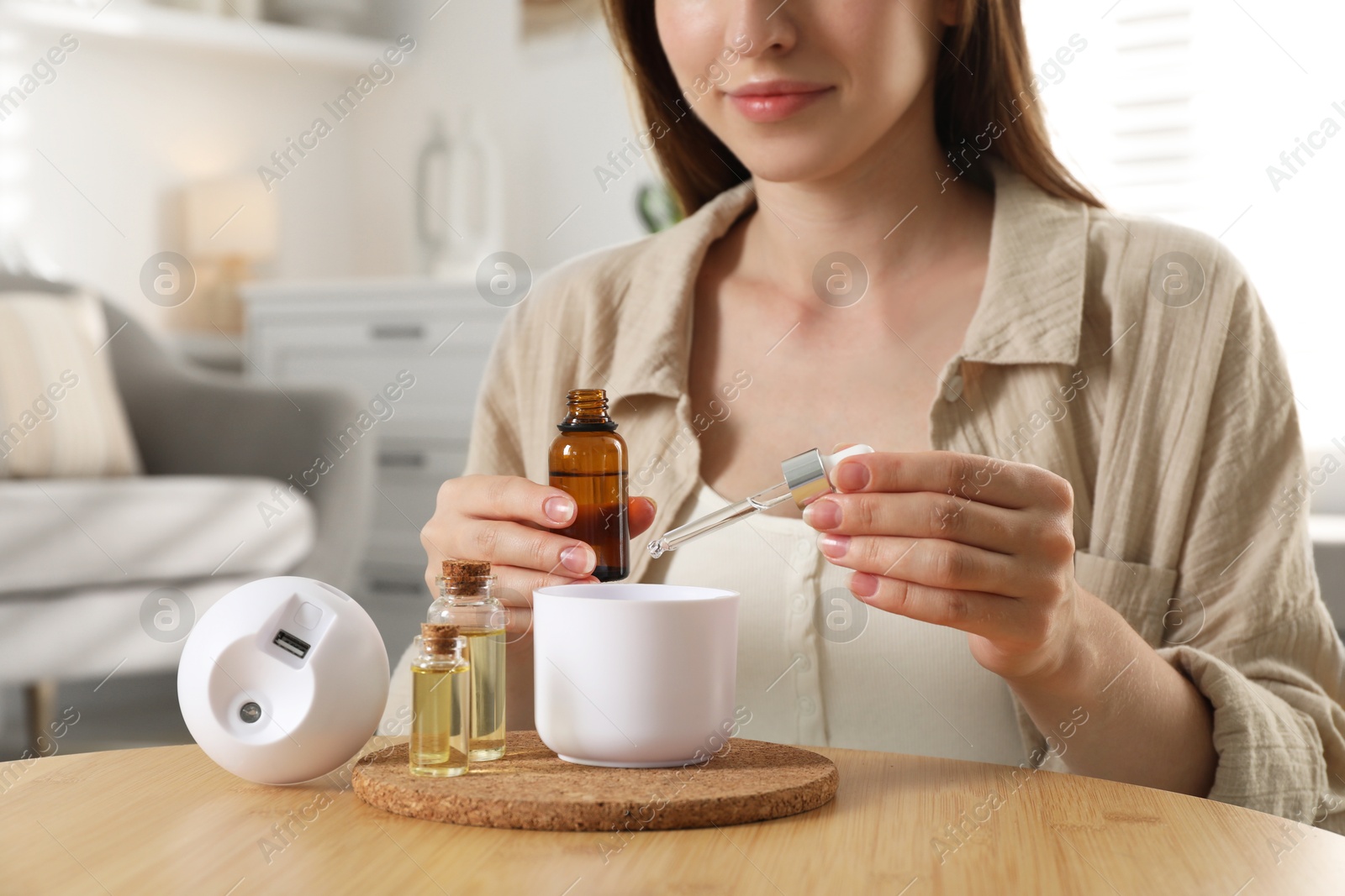 Photo of Woman adding essential oil to aroma diffuser at home, closeup