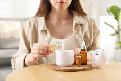 Woman adding essential oil to aroma diffuser at home, closeup