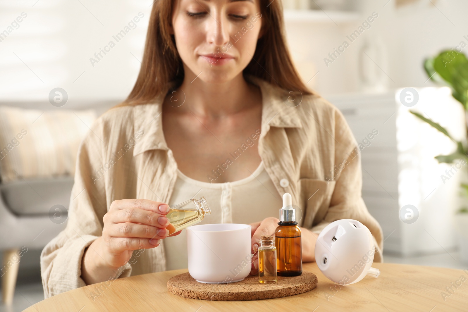 Photo of Woman adding essential oil to aroma diffuser at home