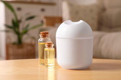 Aroma diffuser and bottles of essential oils on wooden table at home