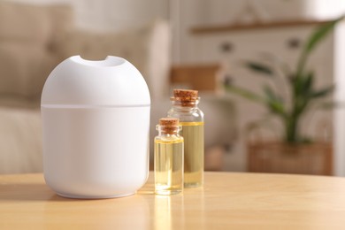 Photo of Aroma diffuser and bottles of essential oils on wooden table at home