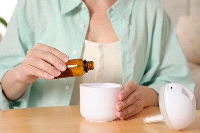 Photo of Woman adding essential oil to aroma diffuser at home, closeup