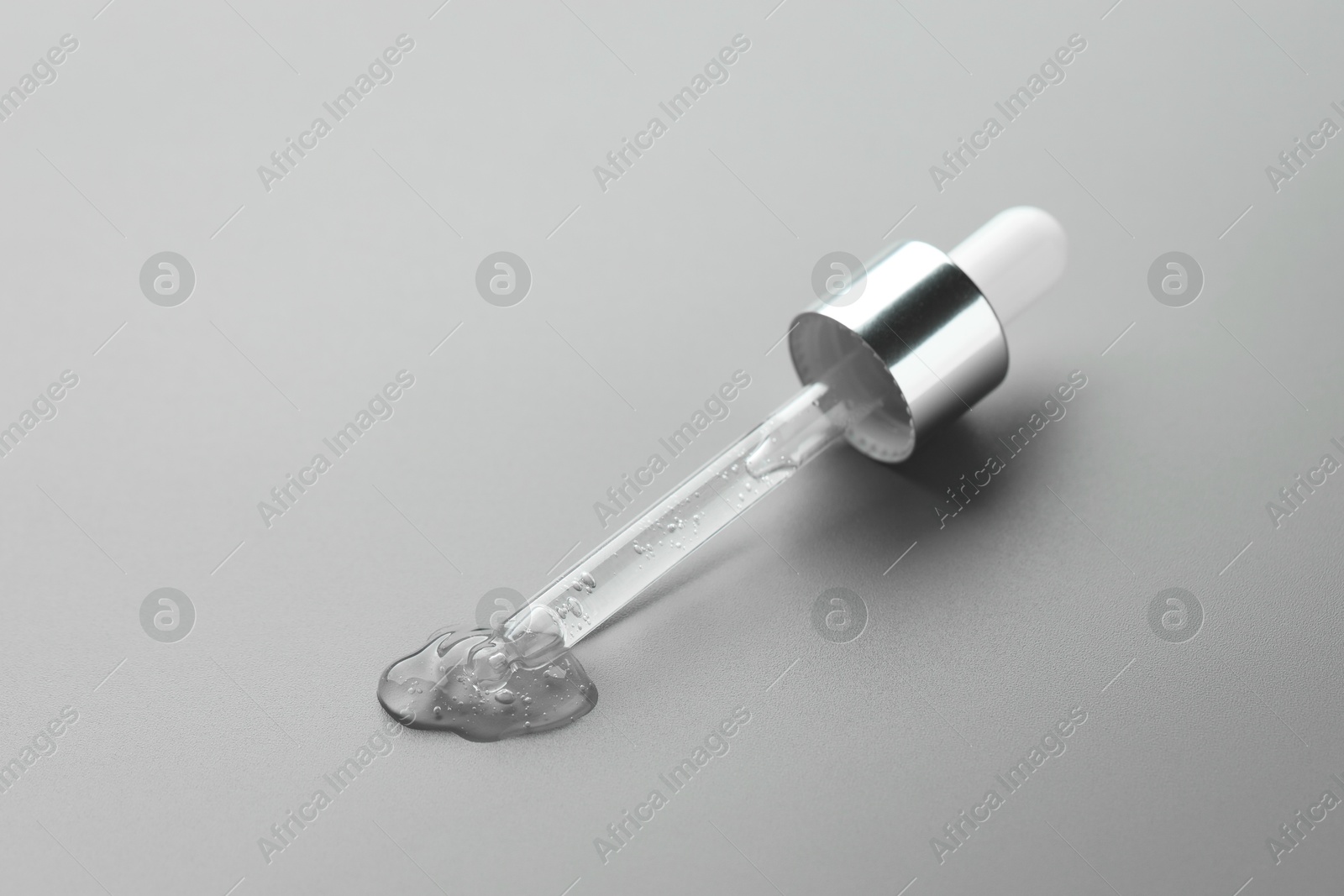 Photo of Dripping cosmetic serum from pipette on grey background