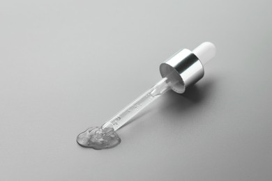 Dripping cosmetic serum from pipette on grey background