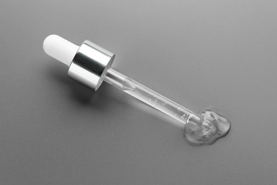 Dripping cosmetic serum from pipette on grey background, above view