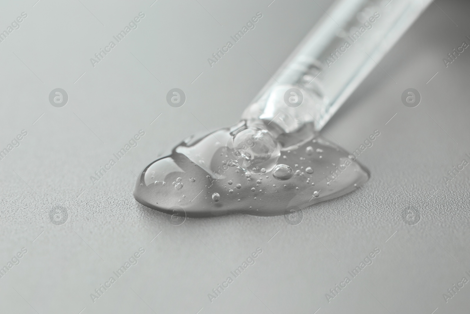 Photo of Dripping cosmetic serum from pipette on grey background, closeup