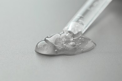 Dripping cosmetic serum from pipette on grey background, closeup