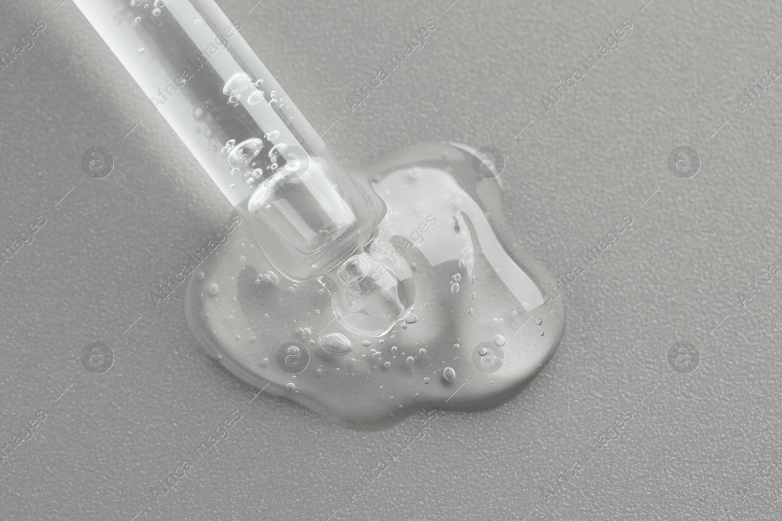 Photo of Dripping cosmetic serum from pipette on grey background, top view