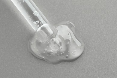 Photo of Dripping cosmetic serum from pipette on grey background, top view