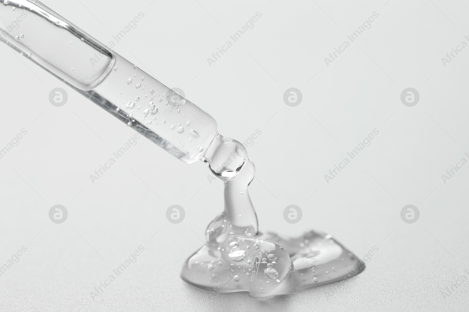 Photo of Dripping cosmetic serum from pipette on grey background, closeup