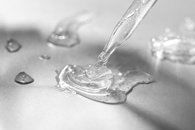 Photo of Dripping cosmetic serum from pipette on grey background, closeup