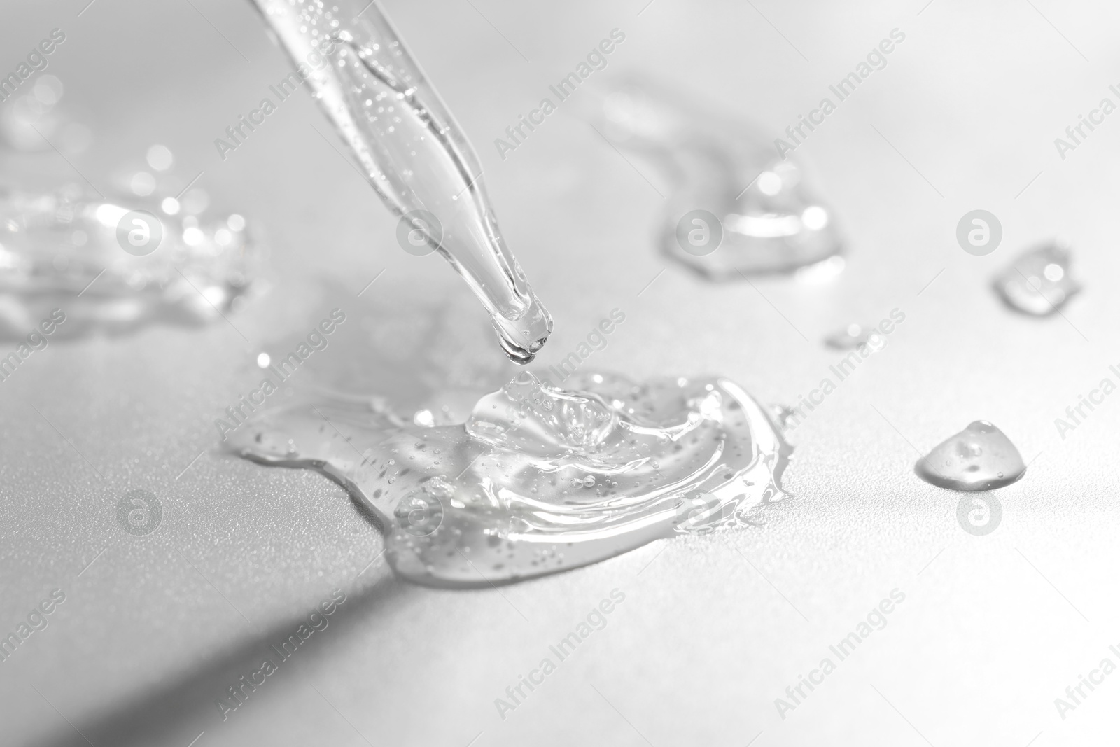 Photo of Dripping cosmetic serum from pipette on grey background, closeup