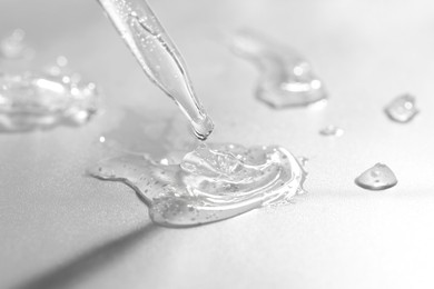 Photo of Dripping cosmetic serum from pipette on grey background, closeup