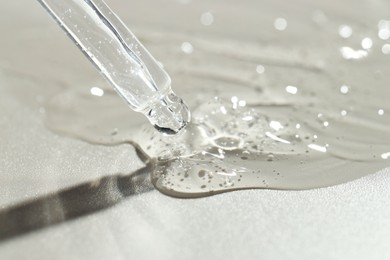 Photo of Dripping cosmetic serum from pipette on grey background, closeup