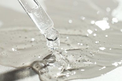 Dripping cosmetic serum from pipette on grey background, closeup