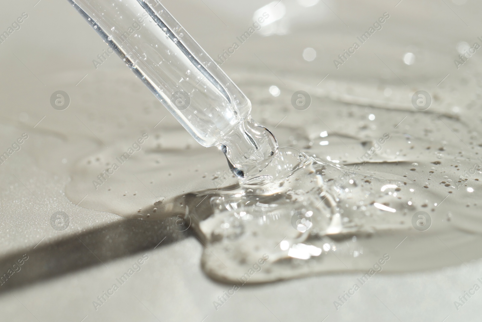 Photo of Dripping cosmetic serum from pipette on grey background, closeup