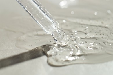 Dripping cosmetic serum from pipette on grey background, closeup